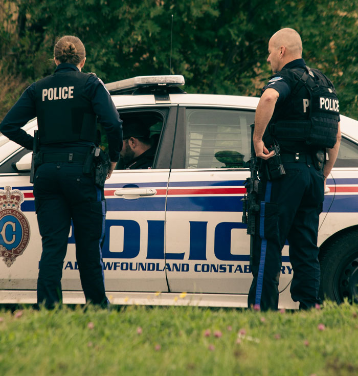 Two police officers standing near a Newfoundland Constabulary police car addressing a suspicious situation. Two police officers standing near a Newfoundland Constabulary police car addressing a suspicious situation.