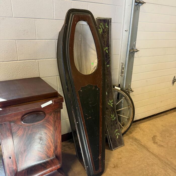 Vintage secondhand finds including a wooden coffin-shaped mirror and antique cabinet in a storage space.