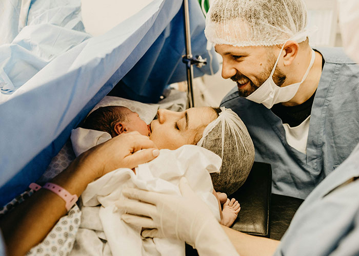Father experiencing the birthing room moment for the first time, watching mother hold newborn baby after delivery.