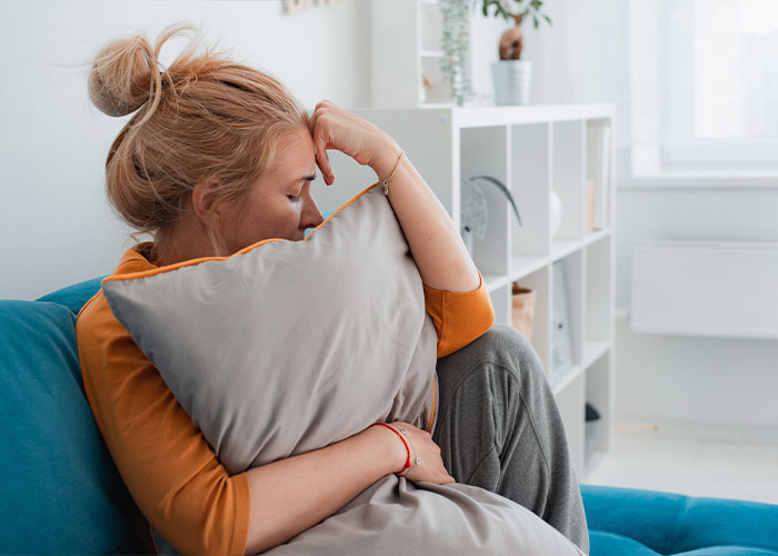 Woman sitting on a couch hugging a pillow, reflecting on creepy facts that might get stuck in the brain forever.