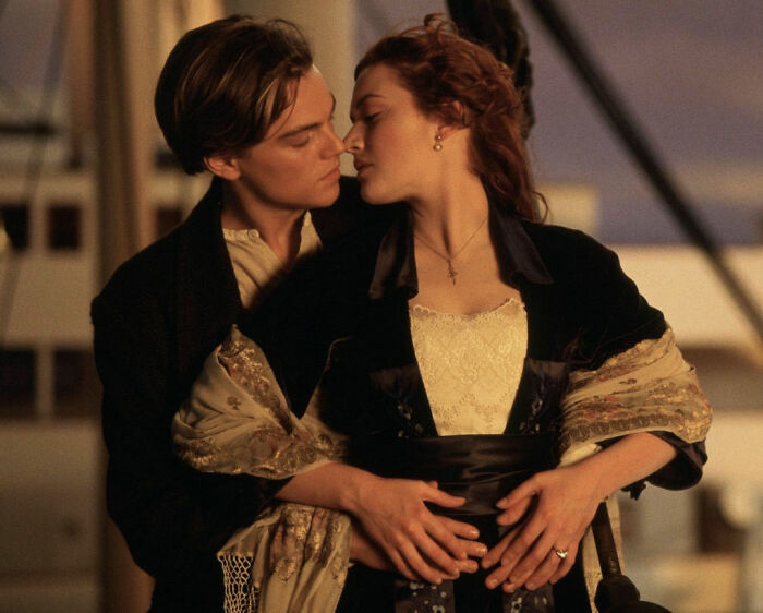 Romantic scene from The Notebook with a couple embracing closely on a ship deck at sunset, showing intimate connection.