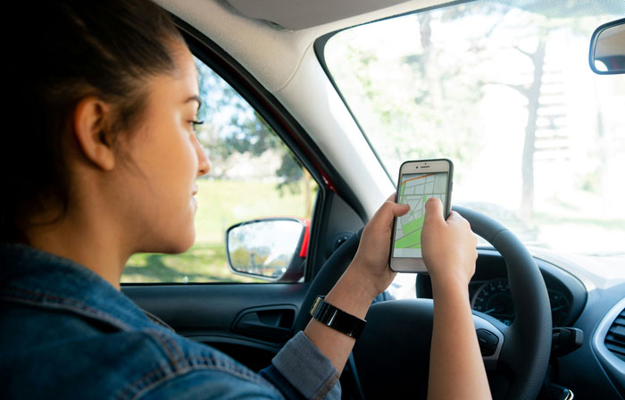 Woman in a car using a smartphone navigation app, highlighting toxic dating trends people accept as normal behavior.