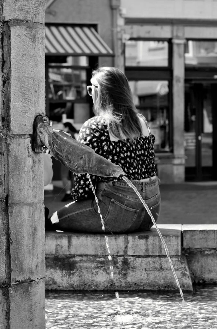 Black and white street shot of a woman sitting by a fountain, capturing the poetry of everyday life in the city.