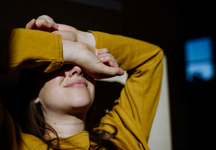 Woman in a yellow shirt shielding her face from light, symbolizing regret and reflection on biggest life mistakes.