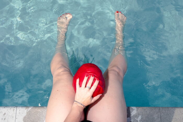 Person with red swim cap sitting by pool with legs in water, capturing a perfectly-timed street photo moment.