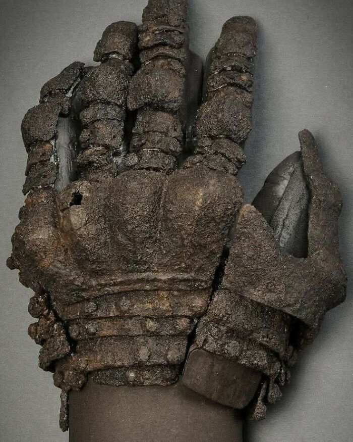 Rusty medieval iron gauntlets laid out on a grey surface, showcasing detailed armor craftsmanship in archaeology.