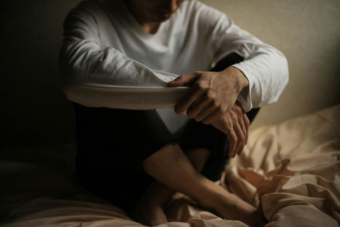 A person sitting on a bed with arms crossed, appearing deep in thought during a therapy session revelation.