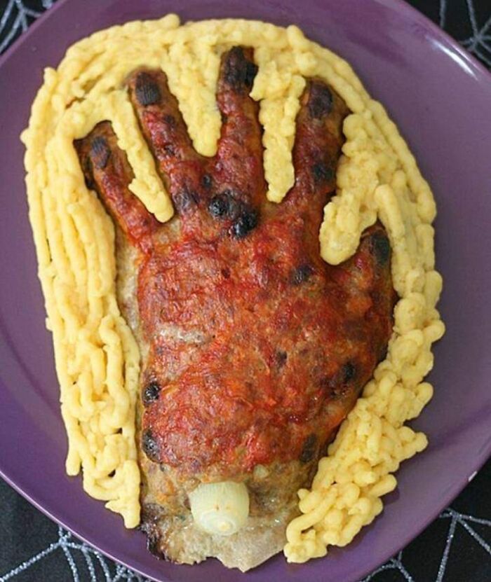 Cursed food shaped like a burnt hand with cheese details on a purple plate, showcasing bizarre and unsettling edible art.