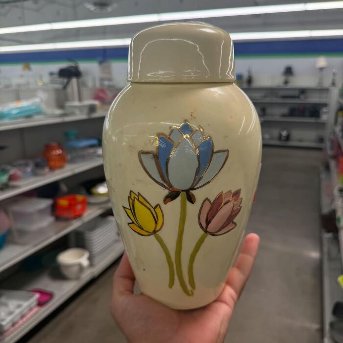 Hand holding a vintage ceramic jar with floral design among cool secondhand finds on store shelves.