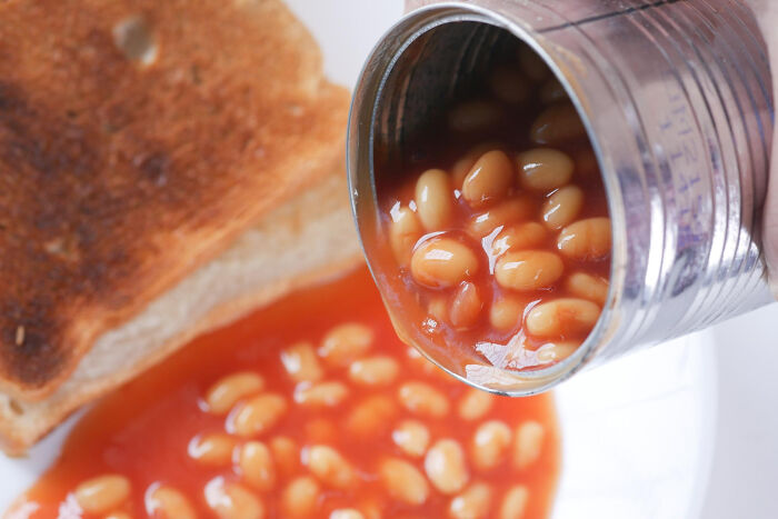 Can of processed baked beans pouring onto a plate with toast, illustrating best processed foods for weight loss.