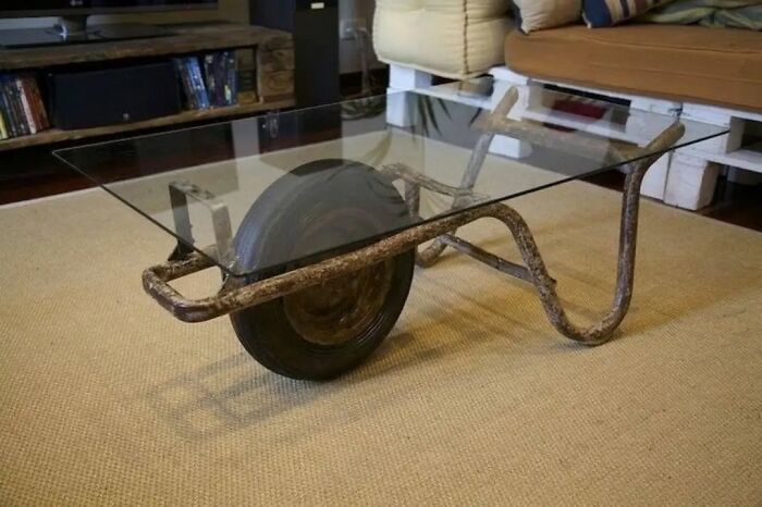 Rusty wheelbarrow repurposed as a glass coffee table, an example of horrendous DIY projects that needed craft shaming.