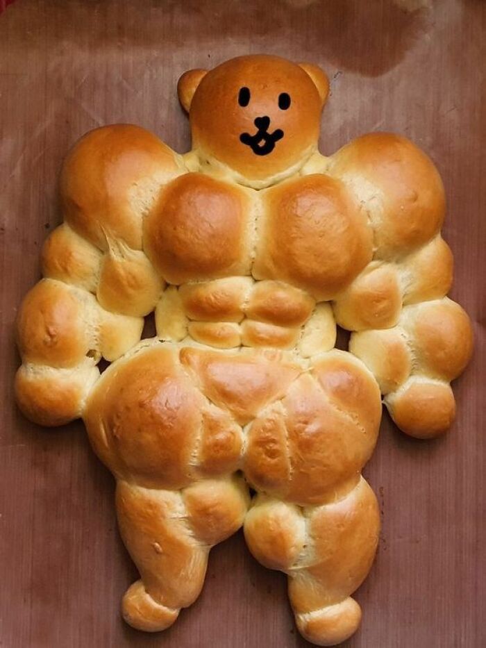Muscular human-shaped bread with a drawn face on a wooden surface, a cursed picture of food that might make you go eeeeeuw.