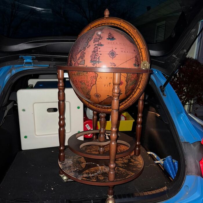 Vintage wooden globe bar cart inside a car trunk, showcasing a cool secondhand find for home decor enthusiasts.