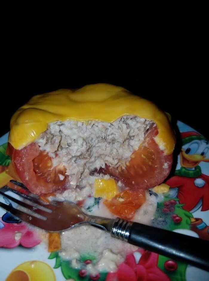 Tomato stuffed with tuna and topped with melted cheese, displayed on a colorful plate, a cursed picture of food.
