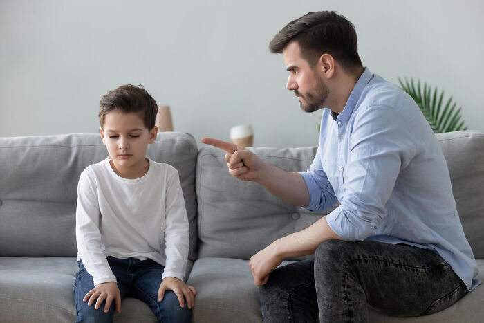 Man pointing and lecturing young boy on a couch showing signs of difficult childhood challenges and emotions.