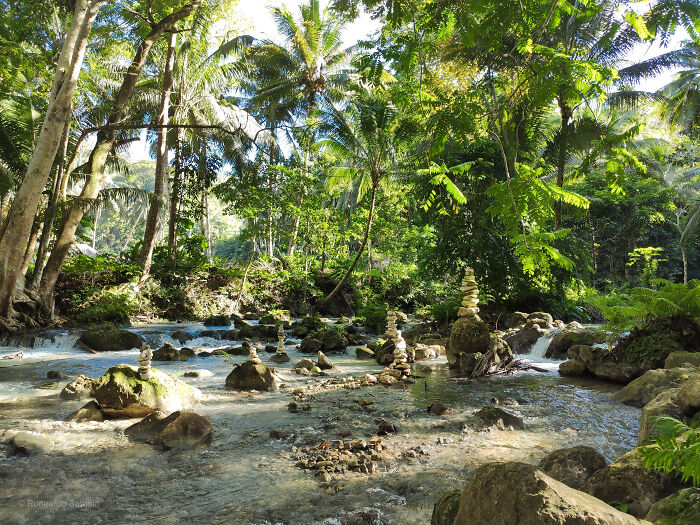 Lush tropical forest with a clear river and stacked balancing rocks showcasing breathtaking travel photography.