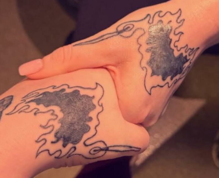 Two hands with matching tattoos featuring black ink designs surrounded by flames, showcasing hilariously bad tattoos.