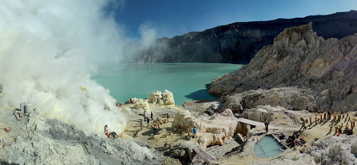 Steamy volcanic crater lake with rugged rocky terrain and small groups of travelers at one of the scariest places around the world.