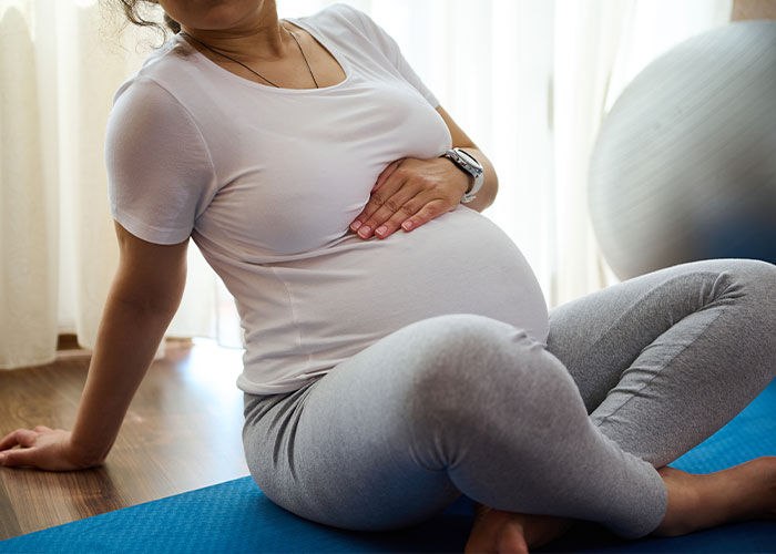 Pregnant woman sitting on exercise mat holding her belly, illustrating creepy facts that might get stuck in your brain.