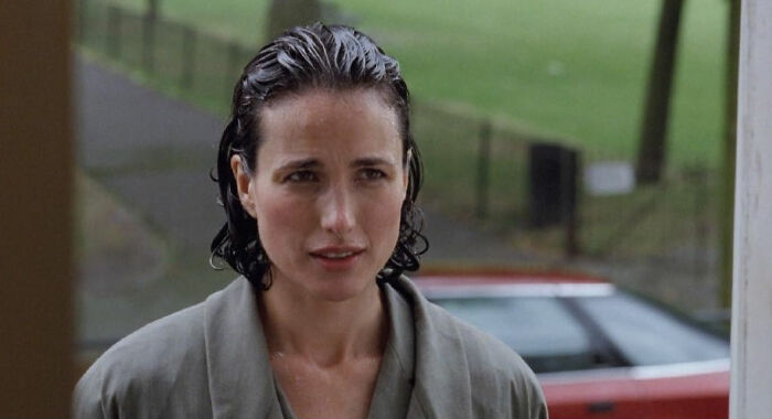 Woman with wet hair wearing a gray robe standing outdoors near a window in a scene depicting toxic romantic movies.
