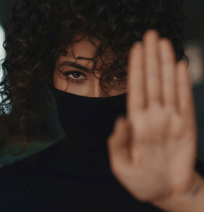 Woman with curly hair wearing a black turtleneck, holding up her hand as a stop gesture, representing toxic dating trends.
