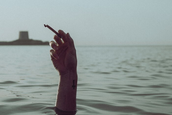 Hand emerging from water holding a burning cigarette, captured in a perfectly-timed street photo by Luca Regoli.