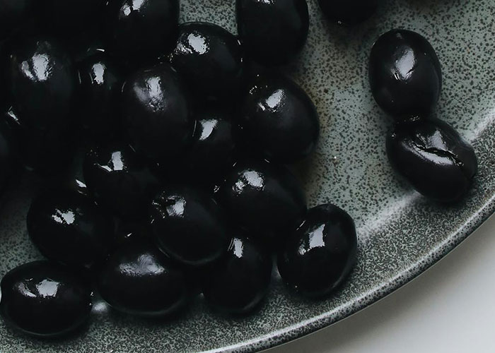 Glossy black olives piled on a textured gray plate, illustrating a common buffet food item in food service encounters.