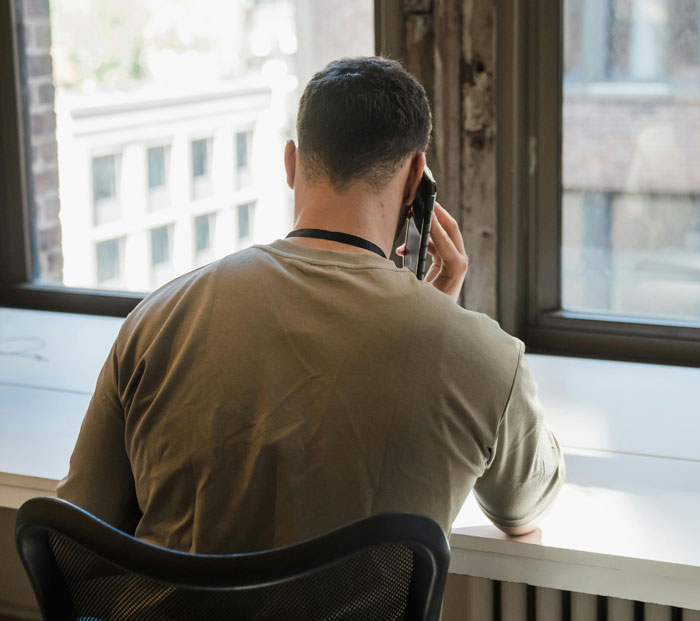 Man talking on phone at desk near window, illustrating poor parenting and custody issues related to babysitting kids.