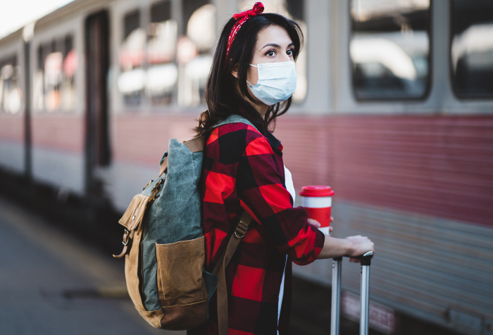 Woman wearing face mask with luggage at train station, symbolizing best countries to live in 2025 travel and safety.
