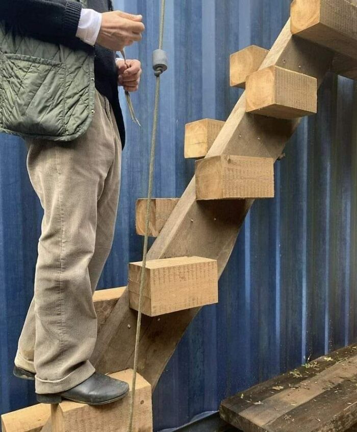 Man standing on dangerous makeshift death stairs with uneven wooden steps against a blue corrugated wall.