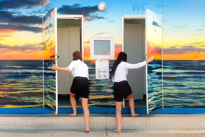 Two women opening restroom doors with ocean sunset mural in background, captured by street photographer.