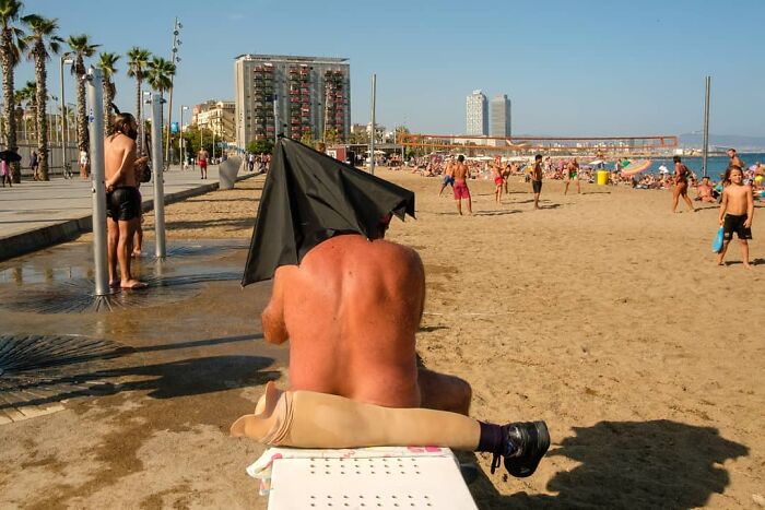 Candid street photo of a man at the beach with an umbrella over his head, capturing an unusual moment by an award-winning photographer.