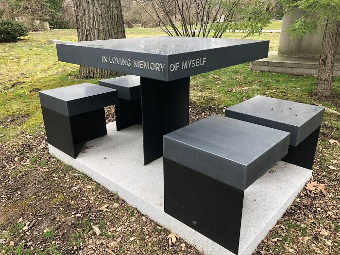 Modern black stone memorial bench and table in a park setting with the phrase In loving memory of myself engraved on it.