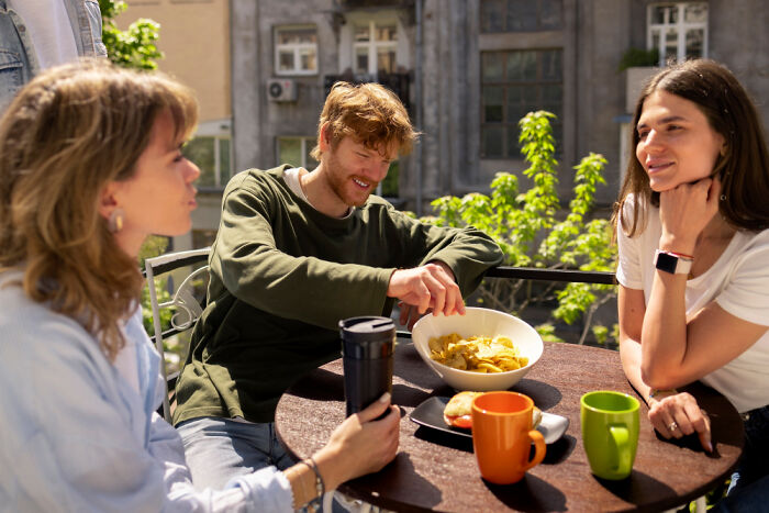 Three friends enjoying snacks and drinks outdoors, sharing travel hacks tips on a sunny day.