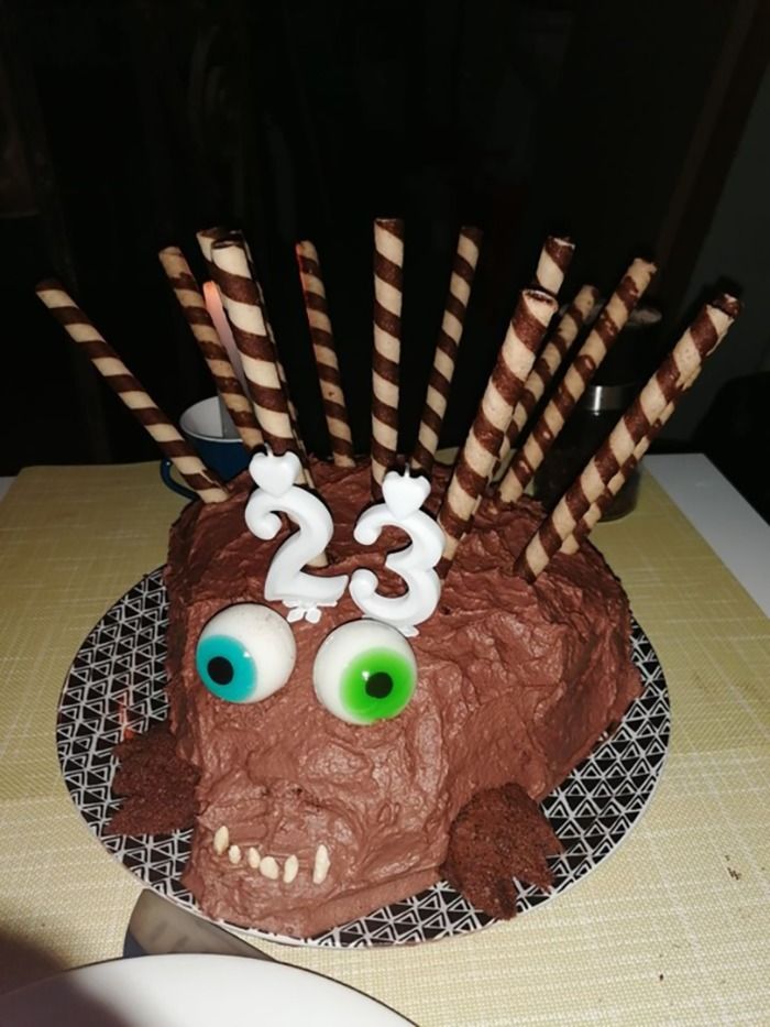 Chocolate cake shaped like a creepy creature with candy eyes and striped wafer sticks, a cursed picture of food photograph.