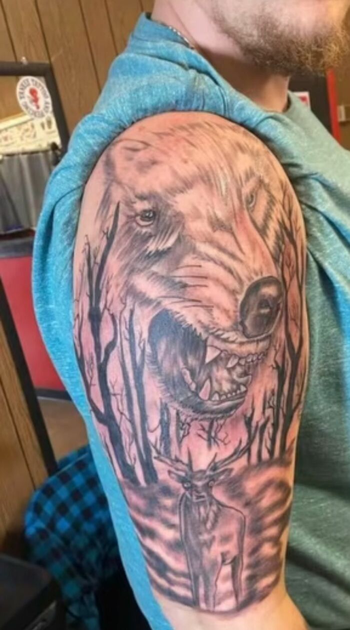 Tattoo on arm showing a snarling wolf with trees and a deer, an example of hilariously bad tattoos people didn’t realize.