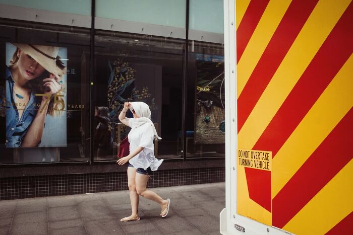 Woman walking on city sidewalk near bright yellow and red truck in candid street photo by Alex McClintock.