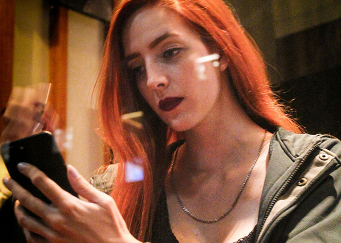 Young woman with red hair looking at her phone during an awkward date, capturing the painful and awkward dating moments.