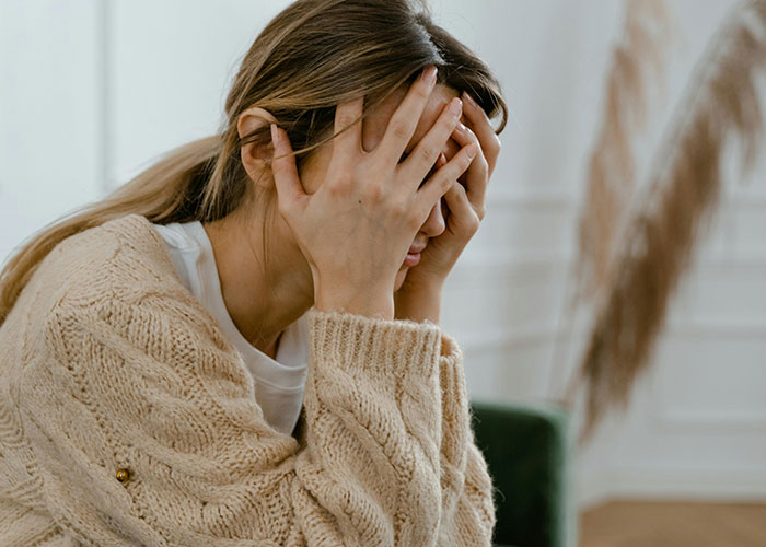 A woman in a beige sweater covering her face with her hands, expressing distress after calling off her engagement.