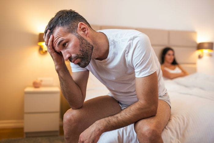 Man sitting on bed looking stressed with woman in background, illustrating biggest mistake of their lives concept.