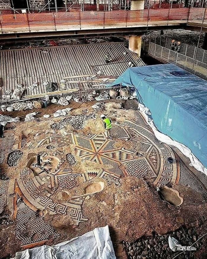 Archaeology world excavation site revealing an intricate ancient mosaic floor with workers uncovering historical artifacts.