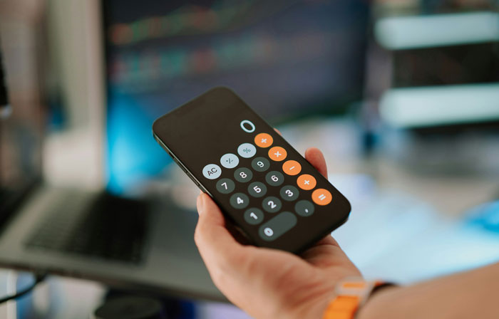 Hand holding smartphone displaying calculator app, illustrating millennials sharing biggest lies they were told growing up.