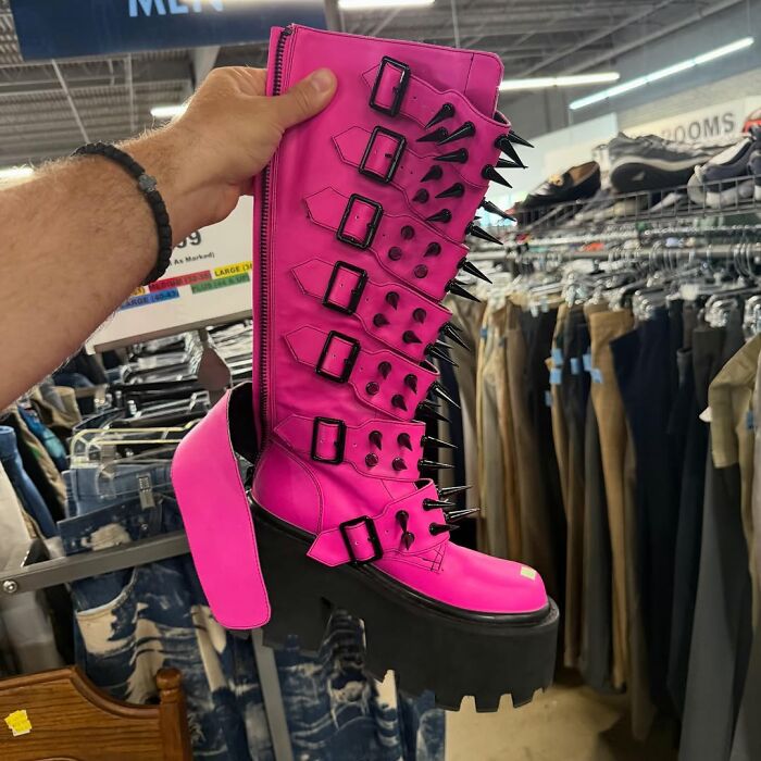 Bright pink platform boot with spikes and buckles held up in a thrift store showcasing cool secondhand finds.