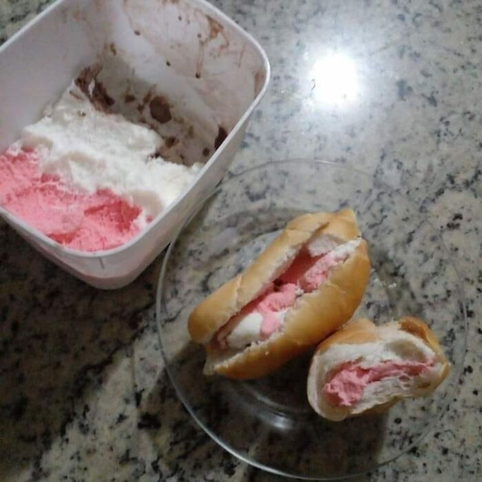 Ice cream scooped into a bread roll on a plate next to a partially used ice cream container, a cursed food picture.