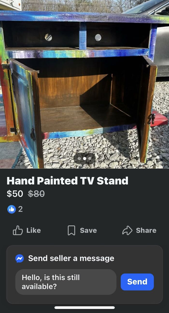Hand painted DIY TV stand with uneven colorful paint job and open cabinet doors on gravel outdoors.