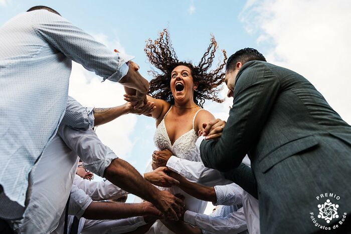 Bride with flowing hair laughing joyfully as friends lift her in an unforgettable wedding photo moment.