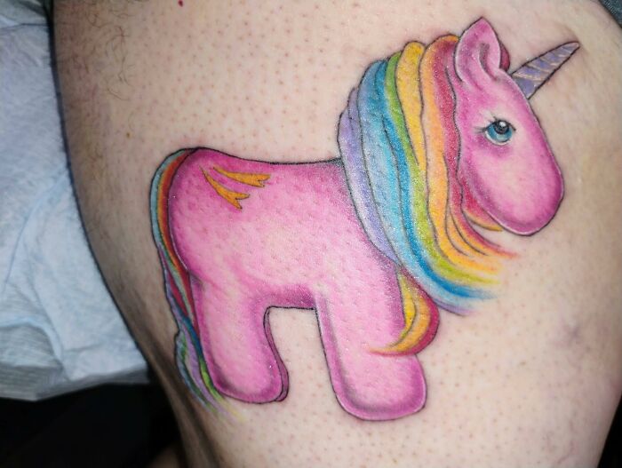 Pink unicorn tattoo with a rainbow mane on skin, an example of hilariously bad tattoos and inkshaming moments.
