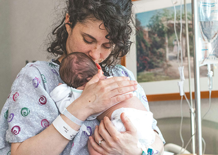 New parent in hospital room holding newborn baby, capturing the first moments inside the birthing room experience.