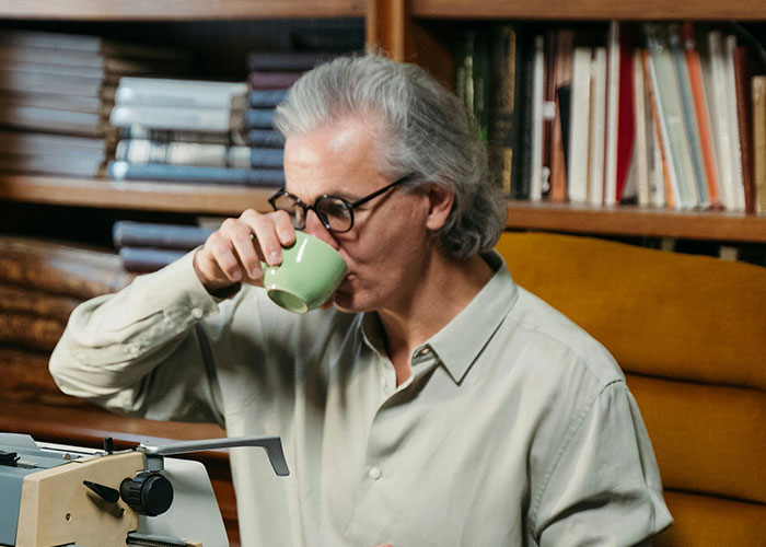 Man with gray hair and glasses drinking coffee near a typewriter in a cozy study, illustrating take one for the team moment.