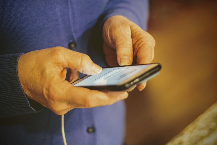 Person wearing a blue sweater using smartphone with focus on hands illustrating toxic dating trends in digital communication.